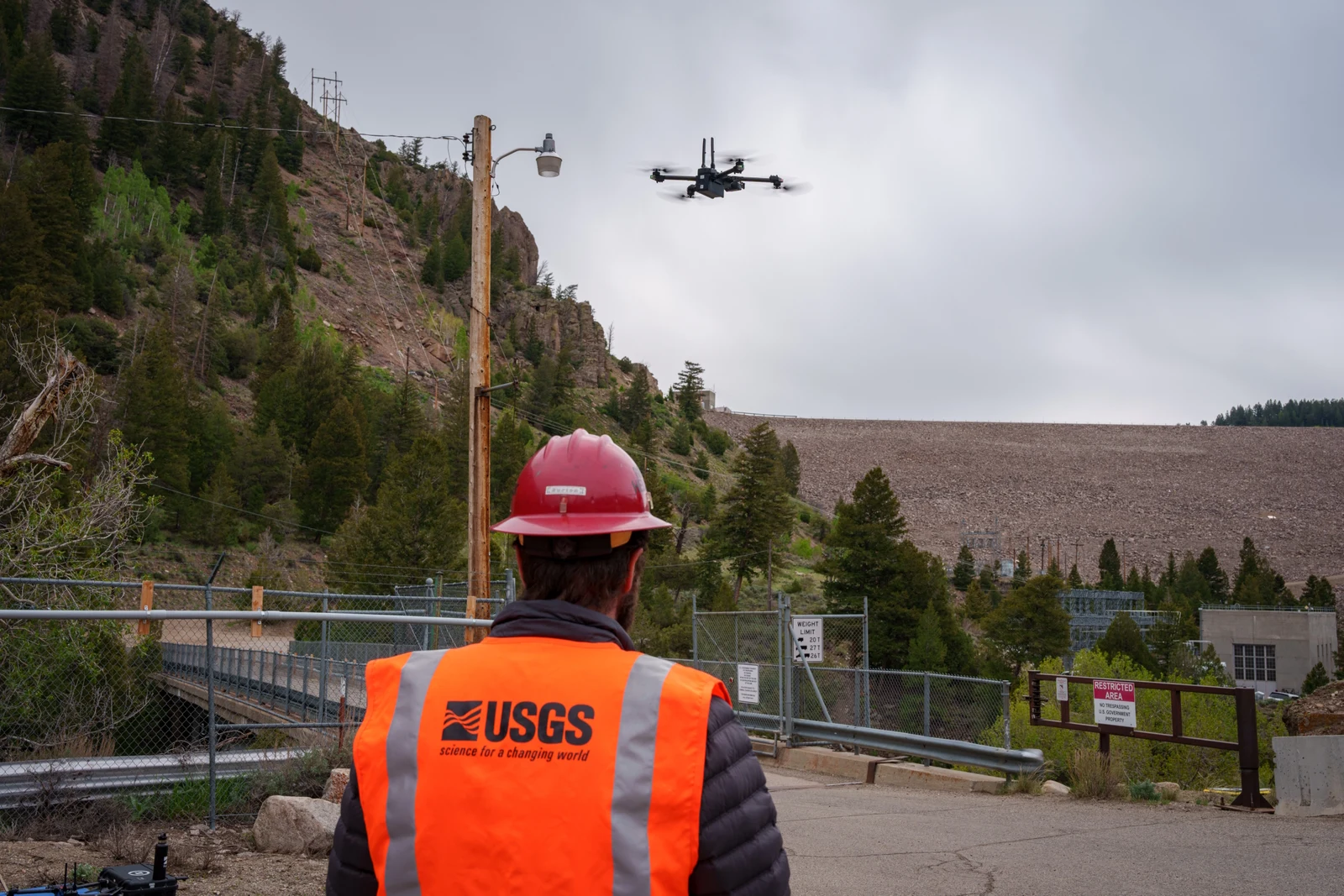USGS remote pilot in high-visibility clothing watches a multirotor UAS near Green Mountain Reservoir infrastructure.