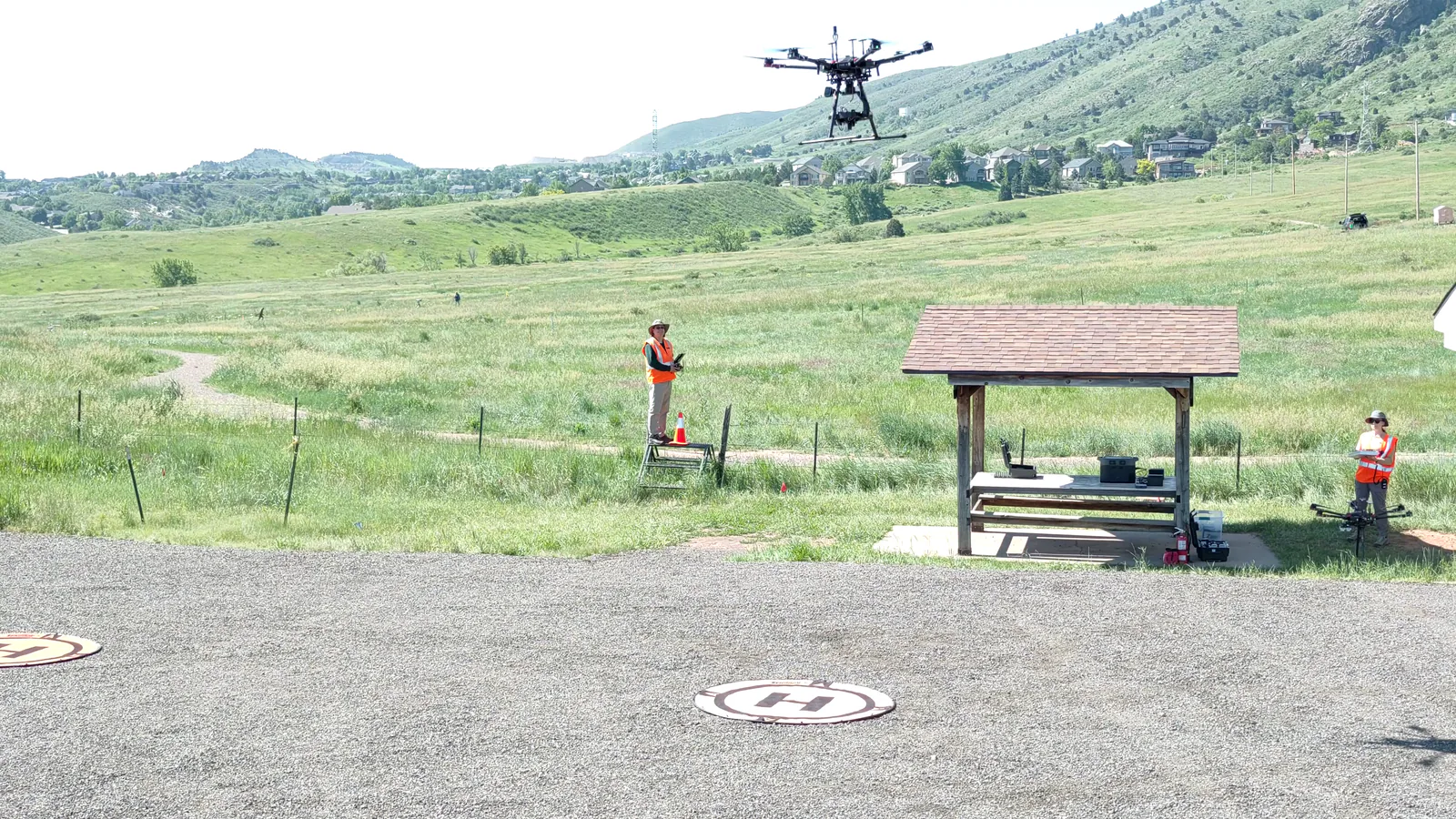 A field crew supervises a multirotor UAS flying above a grassland test area.